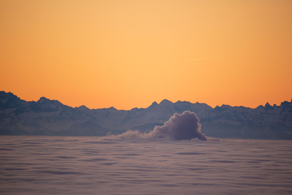 Blick auf die Schweizer Alpen, aus dem Nebelmeer ragt der Dampf aus einem Kernkraftwerk heraus.