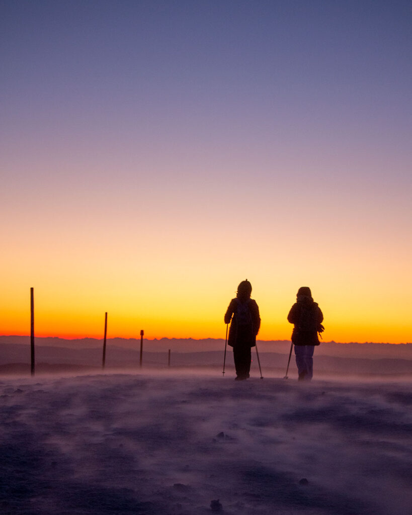 Zwei Menschen mit Wanderstöcken im Schnee auf dem Weg zum Sonnenaufgang