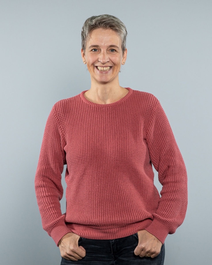 Ada Rhode im rosafarbenen Strickpullover, lächelnd, die Hände in den Hosentaschen