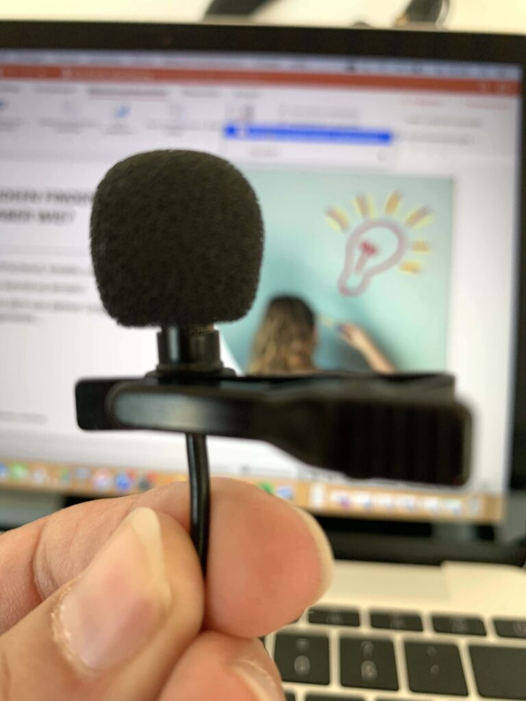 Ansteckmikrofon in der Hand vor einem Laptop mit Präsentationsfolie